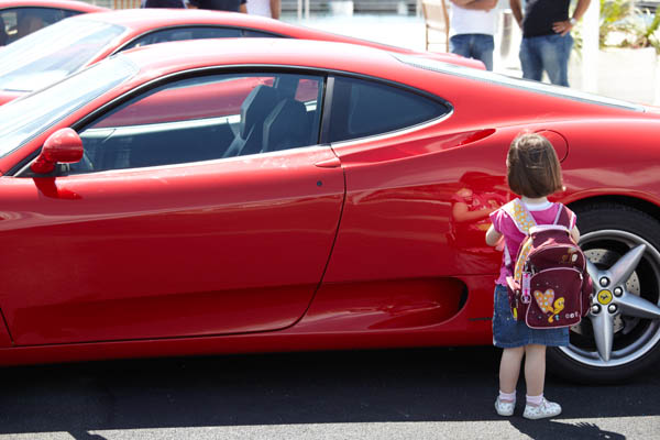 A small girl looking at a red car