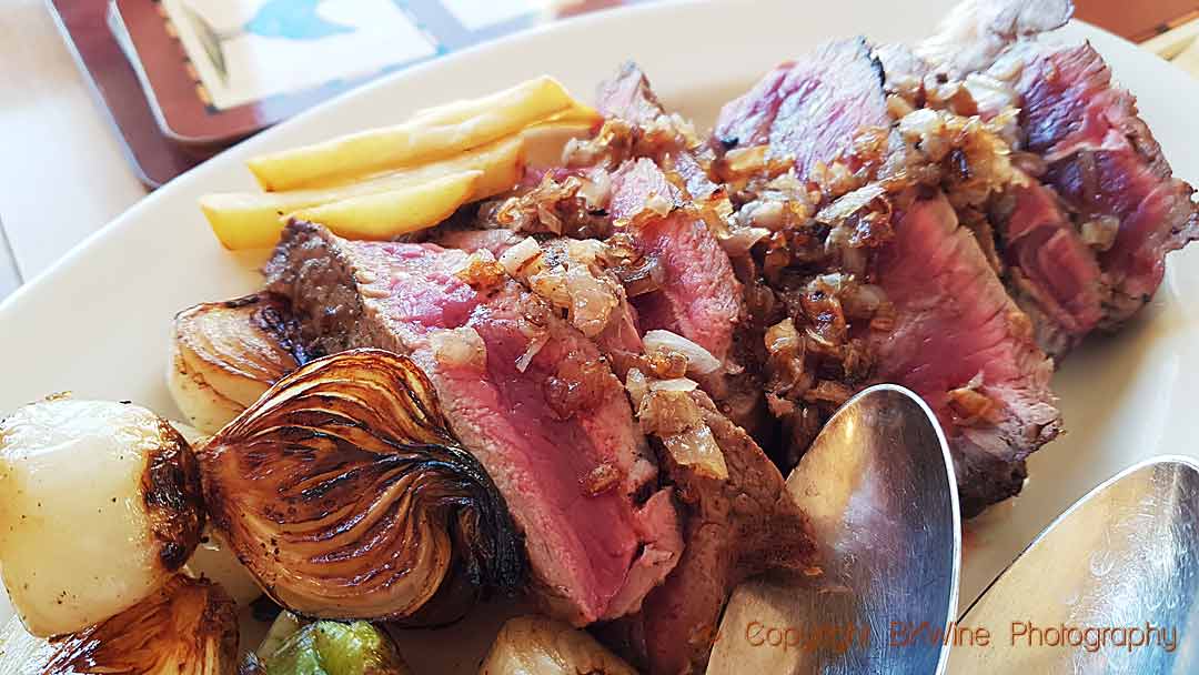 A thick slice of entrecôte, grilled and served with grilled onions and French fries